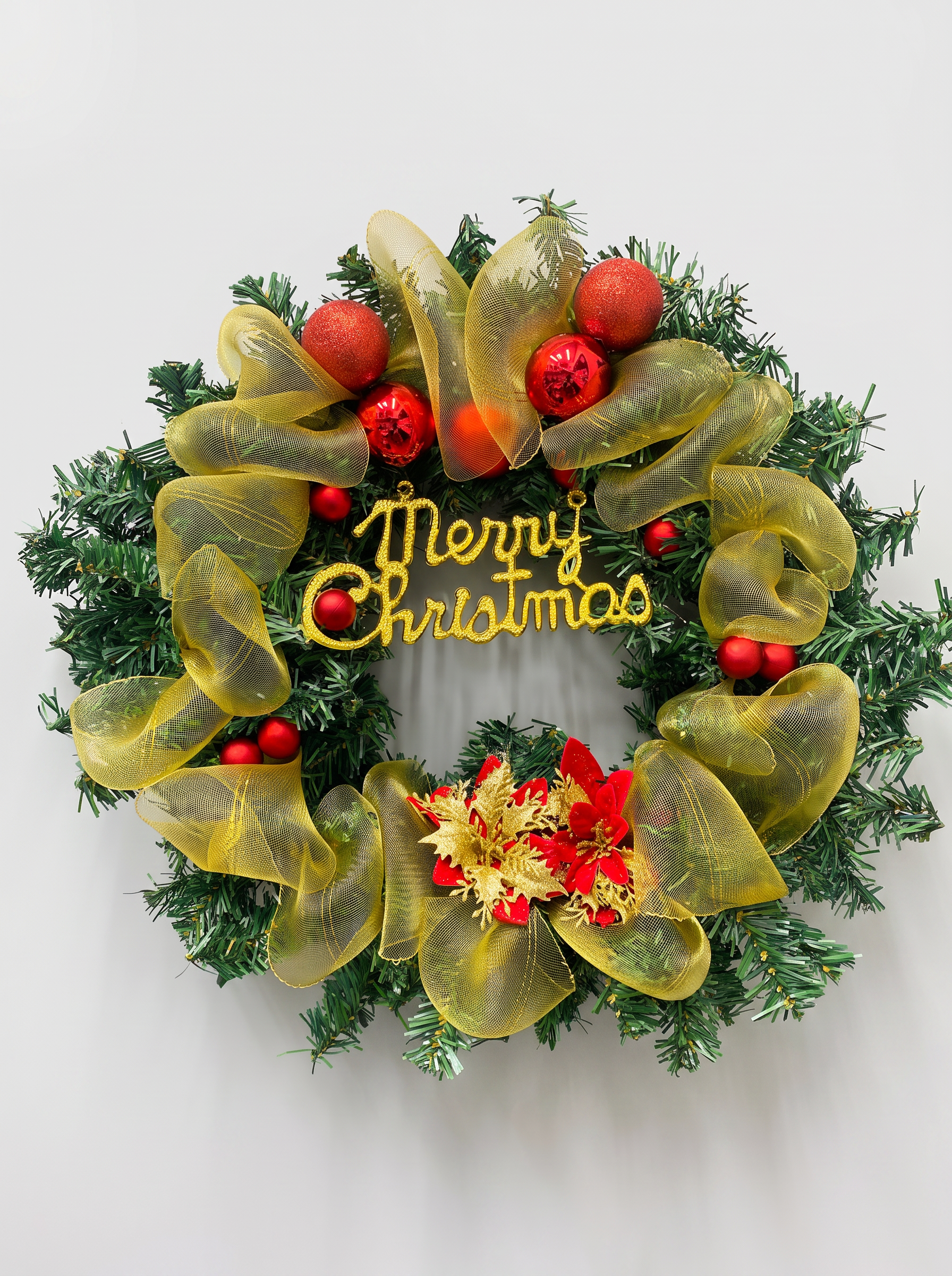 Green evergreen wreath decorated with gold mesh ribbon, red baubles, and Merry Christmas in gold script