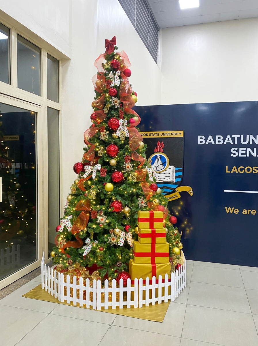 Large Christmas tree in a corporate lobby styled with red and gold ornaments next to a blue university backdrop